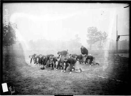 Lake Forest Academy varsity football team crouching in an offensive line formation on an athletic field, dark exposure - Chicago Daily News, Inc.