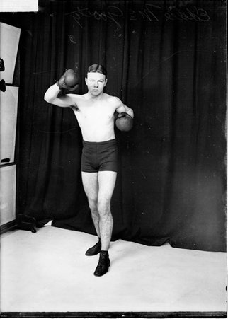 Pugilist, Eddie McGoorty, holding his right hand at head-level and pulling back his left arm, standing in front of a backdrop - Chicago Daily News, Inc.