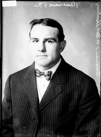 Wrestler Gus (Americus) Schoenle, sitting in front of a light-colored backdrop in a room - Chicago Daily News, Inc.