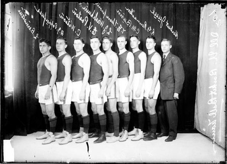 University of Illinois basketball players, one wearing a suit, standing in front of a backdrop - Chicago Daily News, Inc.