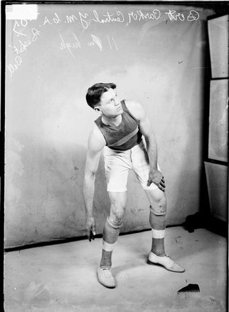 Central YMCA basketball player Bert Parker leaning to his right, standing in front of a light-colored backdrop - Chicago Daily News, Inc.