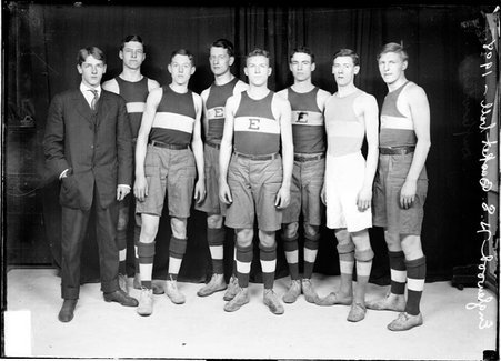 Englewood High School basketball team members standing in front of a dark backdrop in a room - Chicago Daily News, Inc.