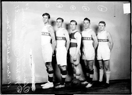 St. Peters basketball players Larsen, John White, Jones, Warren, and Naumann, standing in a single line in front of a backdrop - Chicago Daily News, Inc.
