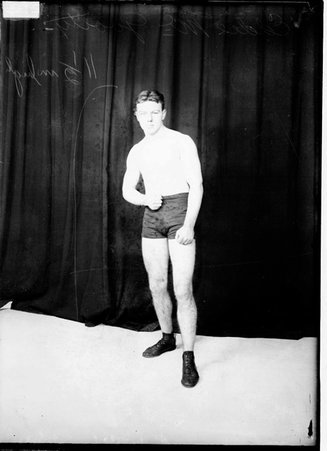 Pugilist Eddie McGoorty, standing in front of a dark backdrop in a room - Chicago Daily News, Inc.