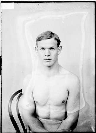 Pugilist Bruno Winkley, sitting shirtless in front of a light-colored backdrop in a room - Chicago Daily News, Inc.