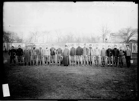 Crane Manual Training High School football team and three men wearing street clothes standing on a football field, dark exposure - Chicago Daily News, Inc.