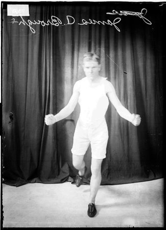 Athlete James A. Brough, holding his hands out at his sides, standing on one foot in front of a dark backdrop - Chicago Daily News, Inc.