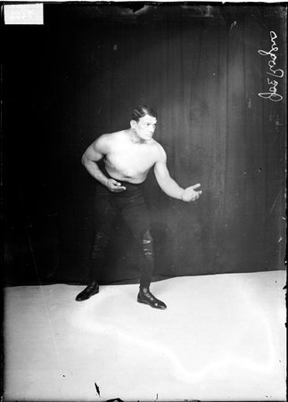 Wrestler Joe Rogers, holding his hands in front of him with palms facing upwards, standing in an athletic stance in front of a backdrop - Chicago Daily News, Inc.