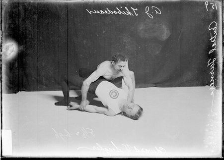 Central Turners wrestlers, A .J. Thibodeaux holding Edward V. Siegler by the shoulder and wrist, crouching in front of a dark backdrop - Chicago Daily News, Inc.