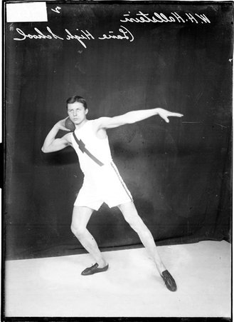 Lane High School athlete W. H. Hallstein, holding a shot put at shoulder height with his right hand, standing in front of a backdrop - Chicago Daily News, Inc.