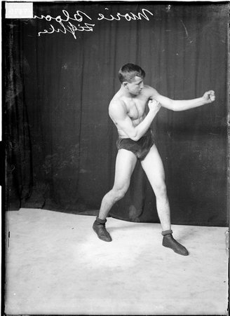 Pugilist Morie Bloom, throwing a left jab, standing in profile in front of a dark backdrop - Chicago Daily News, Inc.