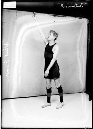 Centennials basketball player Albert Cromer, reaching high with his right hand and arm, standing in front of a light-colored backdrop - Chicago Daily News, Inc.
