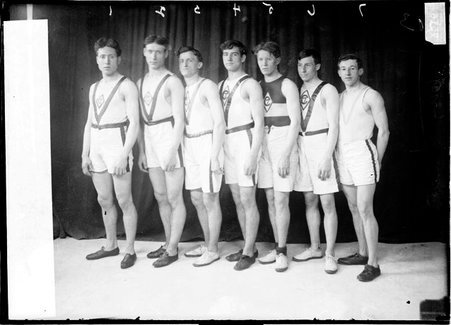 Company C runners Ledford, West, Potter, Donnelly, Dineen, Crocombe, and Dodd standing in front of a dark backdrop - Chicago Daily News, Inc.
