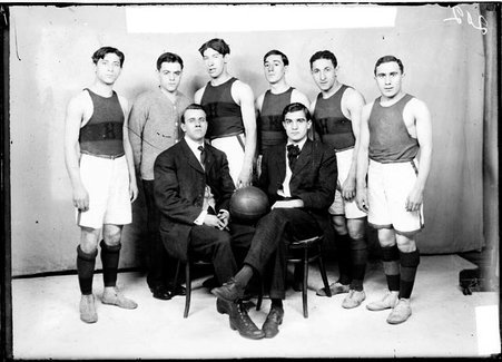 Hull House first basketball team members sitting and standing in front of a light-colored backdrop, light exposure - Chicago Daily News, Inc.