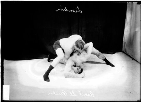 Wrestler Lundin, holding French wrestler Raoul De Rouen in a half-nelson, wrestling on the ground in front of a backdrop - Chicago Daily News, Inc.