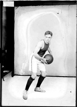 Hull House first team basketball player A. Feinberg, holding a basketball, standing in front of a light-colored backdrop - Chicago Daily News, Inc.