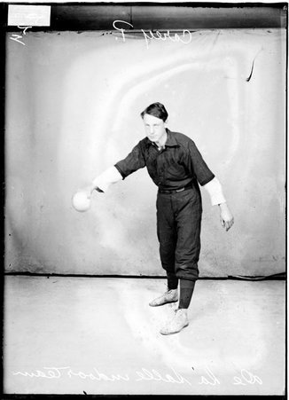 De La Salle indoor baseball player Carey, holding a baseball with his arm extended in front of him, standing in front of a backdrop - Chicago Daily News, Inc.