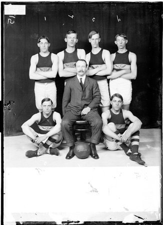 Olivet Centrals basketball players Hild, Peerson, Back, Peterson, Belzer, Pfister, and Lindahl, sitting and standing by a backdrop - Chicago Daily News, Inc.