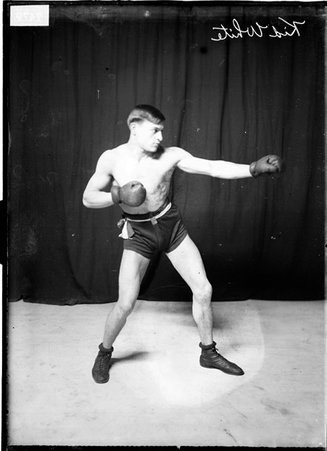 Pugilist Kid White, throwing a left jab, standing in front of a dark backdrop - Chicago Daily News, Inc.
