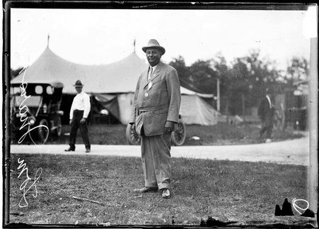 Shooter Tom Marshall, standing on a lawn in front of a sidewalk and a tent at the Chicago Gun Club - Chicago Daily News, Inc.