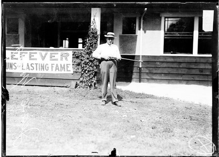Shooter Jesse Young, holding a rifle, standing in front of a low building at the Chicago Gun Club - Chicago Daily News, Inc.