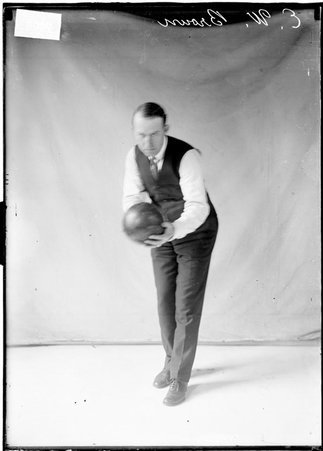 Bowler E. W. Brown, holding a bowling ball in front of him and leaning forward, standing in front of a light-colored backdrop - Chicago Daily News, Inc.