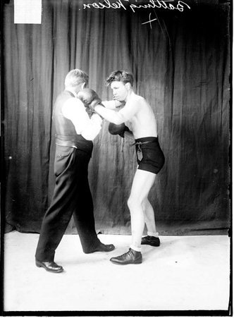 Pugilist Battling Nelson, throwing a left hook at an unidentified man who is wearing street clothes and boxing gloves - Chicago Daily News, Inc.