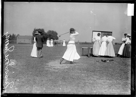 Golfer, Ione Moody, following through after swinging a club, standing on a tee on the grounds of an unidentified golf course - Chicago Daily News, Inc.