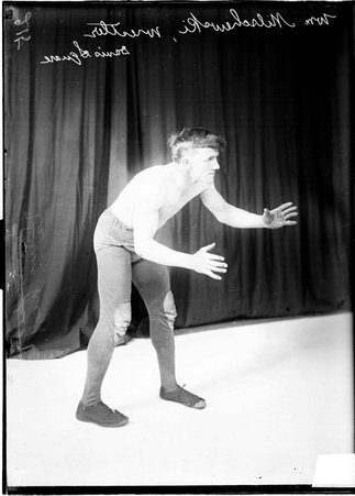 Davis Square wrestler William Milschewski, standing in a ready position in front of a dark backdrop - Chicago Daily News, Inc.
