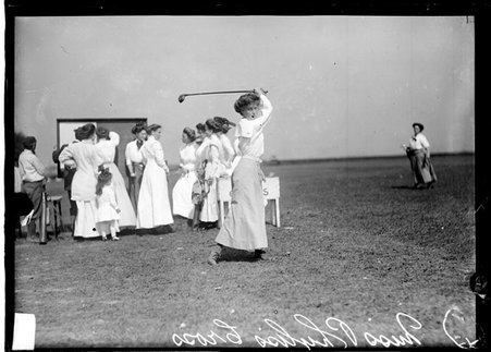 Golfer, Phyliss Cross, following through after swinging a golf club, standing on a tee on the grounds of an unidentified golf course - Chicago Daily News, Inc.