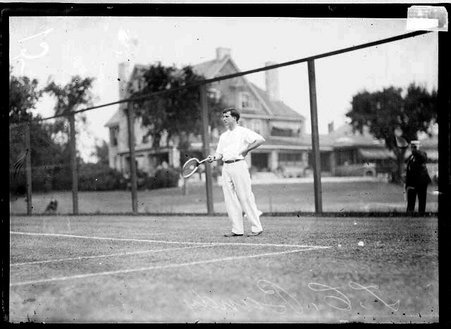 Tennis player, T. C. Bundy, holding a tennis racket in front of him, standing behind the baseline on a tennis court - Chicago Daily News, Inc.