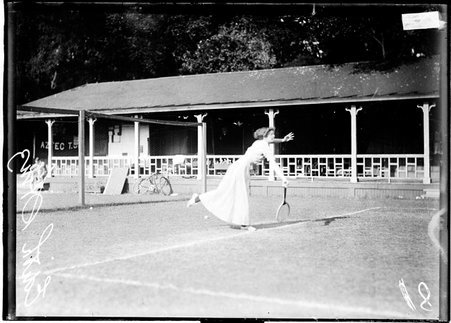 Tennis player, Edith Hinz, following through after swinging a racket, standing on a court at Aztec Tennis Club, dark exposure - Chicago Daily News, Inc.