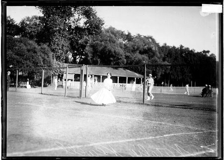 Tennis player, Natalie Newell, holding a tennis racket, standing behind the baseline on a tennis court at the Aztec Tennis Club - Chicago Daily News, Inc.