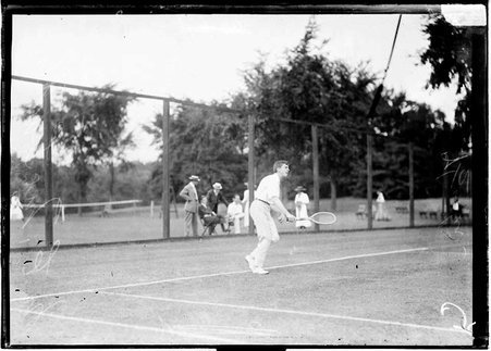 Tennis player, M. E. McLoughlin, holding a tennis racket, standing in front of the baseline on a tennis court - Chicago Daily News, Inc.