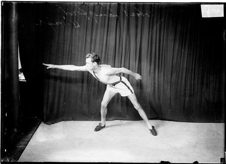 Track athlete, Robert Langford, University High School, leaning over right knee, right arm stretching out in front of dark backdrop - Chicago Daily News, Inc.