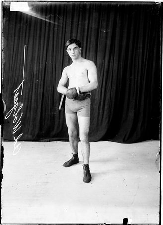Pugilist, Ad. Wolgast, standing with hands on his stomach in front of dark backdrop - Chicago Daily News, Inc.