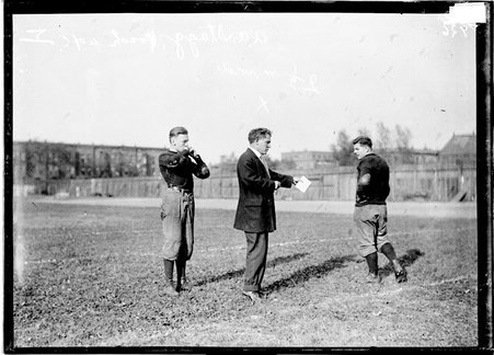 Football, Coach Alonzo A. Stagg standing on grass between two players at Marshall Field, U. of C. - Chicago Daily News, Inc.
