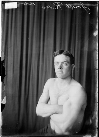 Wrestler, Joseph Rider, sitting with arms crossed on chest in front of dark backdrop - Chicago Daily News, Inc.