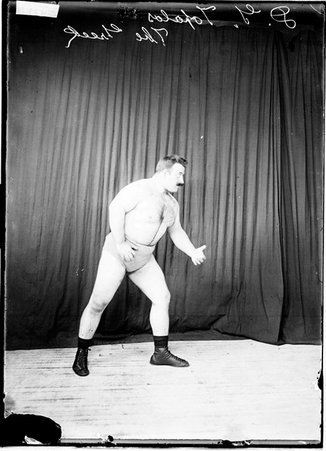 Wrestler, D. G. Topalos, standing with right side to camera and arms at sides against dark backdrop - Chicago Daily News, Inc.