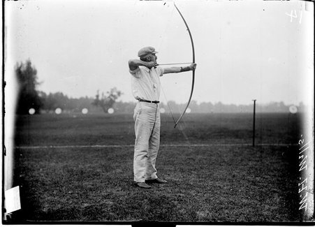Archer, W. H. Wills drawing bow and arrow with point toward right of image at an archery range - Chicago Daily News, Inc.