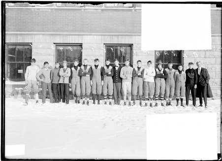 Football team, Curtis High School, seventeen members, standing in snow in front of building - Chicago Daily News, Inc.