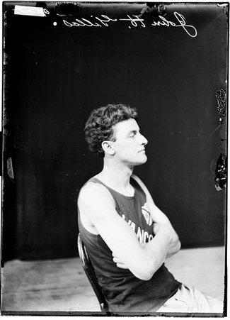 Athlete, John H. Gillas sitting with arms crossed in front of dark backdrop, wearing Vancouver shirt - Chicago Daily News, Inc.