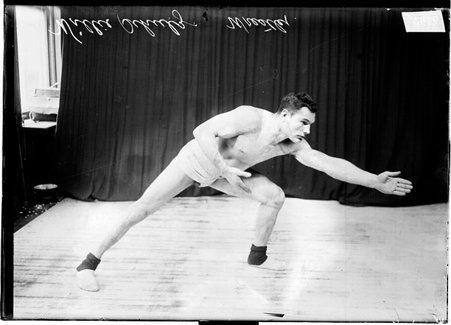 Wrestler Willie Schultz standing in a wrestling stance, lunging to the side on his left leg with his arms stretched to the right of the image - Chicago Daily News, Inc.