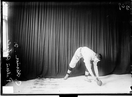 Pilsen Sokols indoor baseball player C. Kermer posing, bending forward at the waist holding a ball in his hands near the floor - Chicago Daily News, Inc.