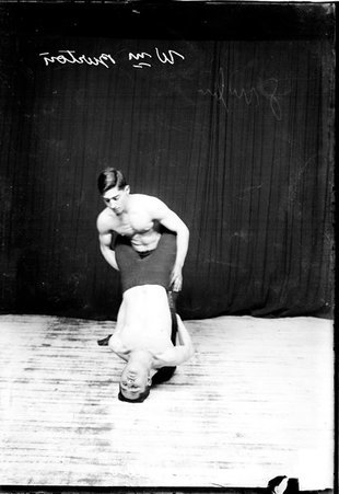 Wrestlers William Burton and Leo Kallis posing on the floor in front of a dark colored background One of the wrestlers supporting himself on his head in front of the other wrestler, who holding his legs. - Chicago Daily News, Inc.