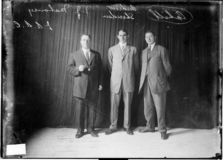 Athletes J. J. Mahoney, Cahill and Andrew Sheridan standing in front of a dark colored background - Chicago Daily News, Inc.