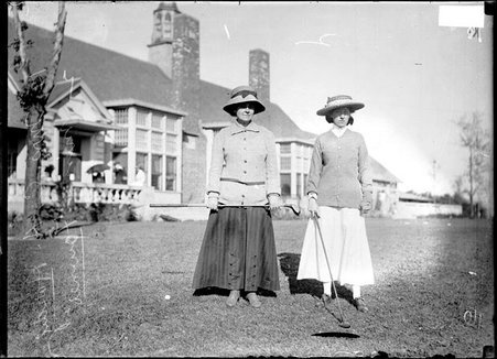 Golfers Mrs. C. A. Hardy and Miss Fownes standing on the grass in front of the clubhouse holding golf clubs at Homewood Golf Links - Chicago Daily News, Inc.