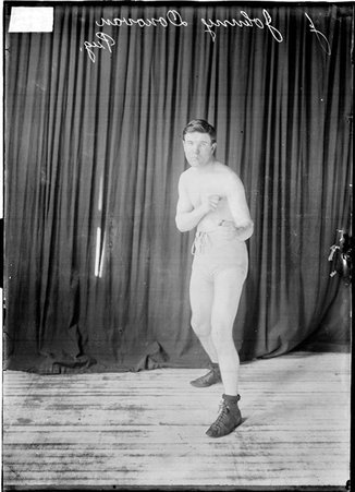 Boxer Johnny Donovan standing in an ordinary boxing stance, facing the camera in front of a dark colored background - Chicago Daily News, Inc.