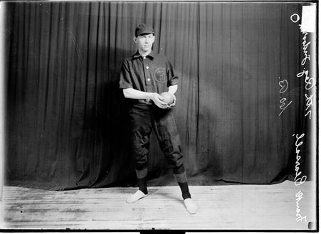 Seventh Regiment indoor baseball player Frank Pearsall holding a ball standing in front of a dark colored background - Chicago Daily News, Inc.