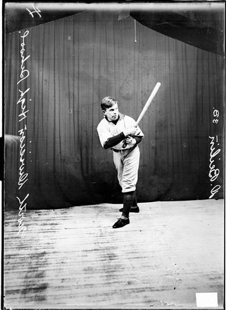 North Division High School indoor baseball player D. Beilin holding a bat standing in front of a dark colored background - Chicago Daily News, Inc.